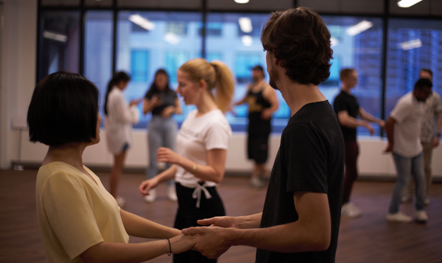 A couple watches attentively as the dance teacher gives instructions during a salsa class at a corporate event taking place in the office's lunch room.